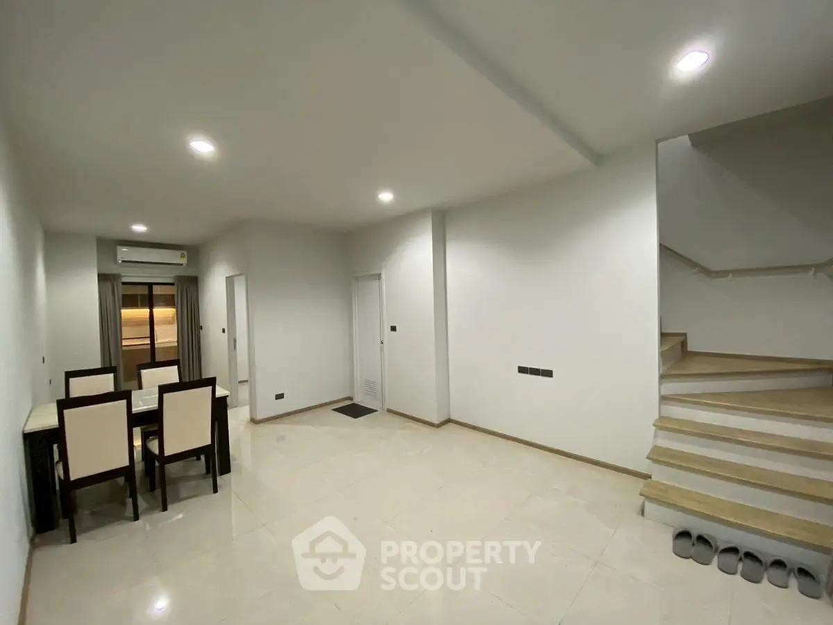 Spacious modern living room with dining area and staircase in a minimalist home.