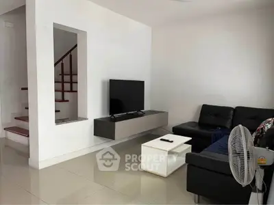 Modern living room with sleek black sofa, wall-mounted TV, and minimalist decor.