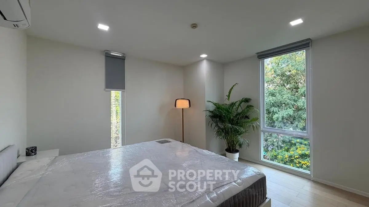 Modern bedroom with large windows and lush greenery view