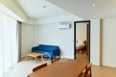 Modern living room with blue sofa and dining area, leading to a cozy bedroom.