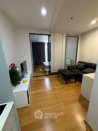 Modern living room with wooden flooring, cozy sofa, and sliding glass doors leading to a bedroom.