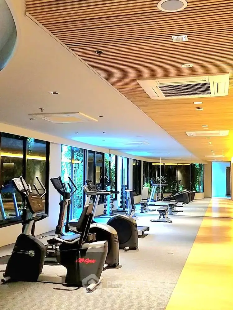 Modern gym with exercise equipment and wooden ceiling in luxury apartment building.