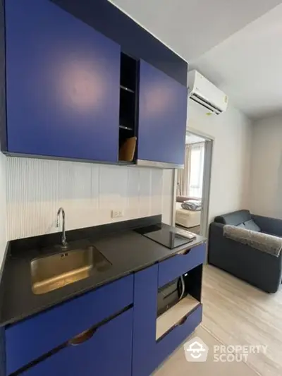 Modern kitchen with sleek blue cabinetry and built-in appliances, seamlessly opening to a cozy living area with comfortable seating and ample natural light.