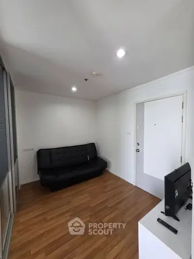 Modern living room with sleek black sofa and wooden flooring, perfect for cozy gatherings.