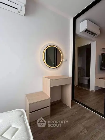 Modern bedroom with stylish vanity and illuminated mirror, featuring sleek wood flooring and air conditioning.