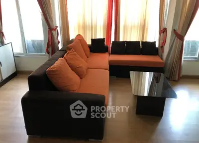 Spacious living room with modern orange and brown sofa, glass coffee table, and elegant curtains.