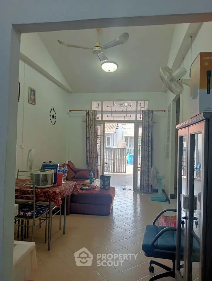 Spacious living room with ceiling fan and natural light, featuring comfortable seating and tiled flooring.