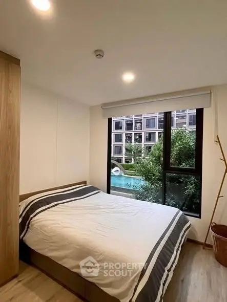 Cozy bedroom with large window overlooking a pool and modern building exterior.