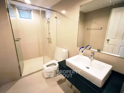 Modern bathroom with glass shower, sleek sink, and neutral tiles