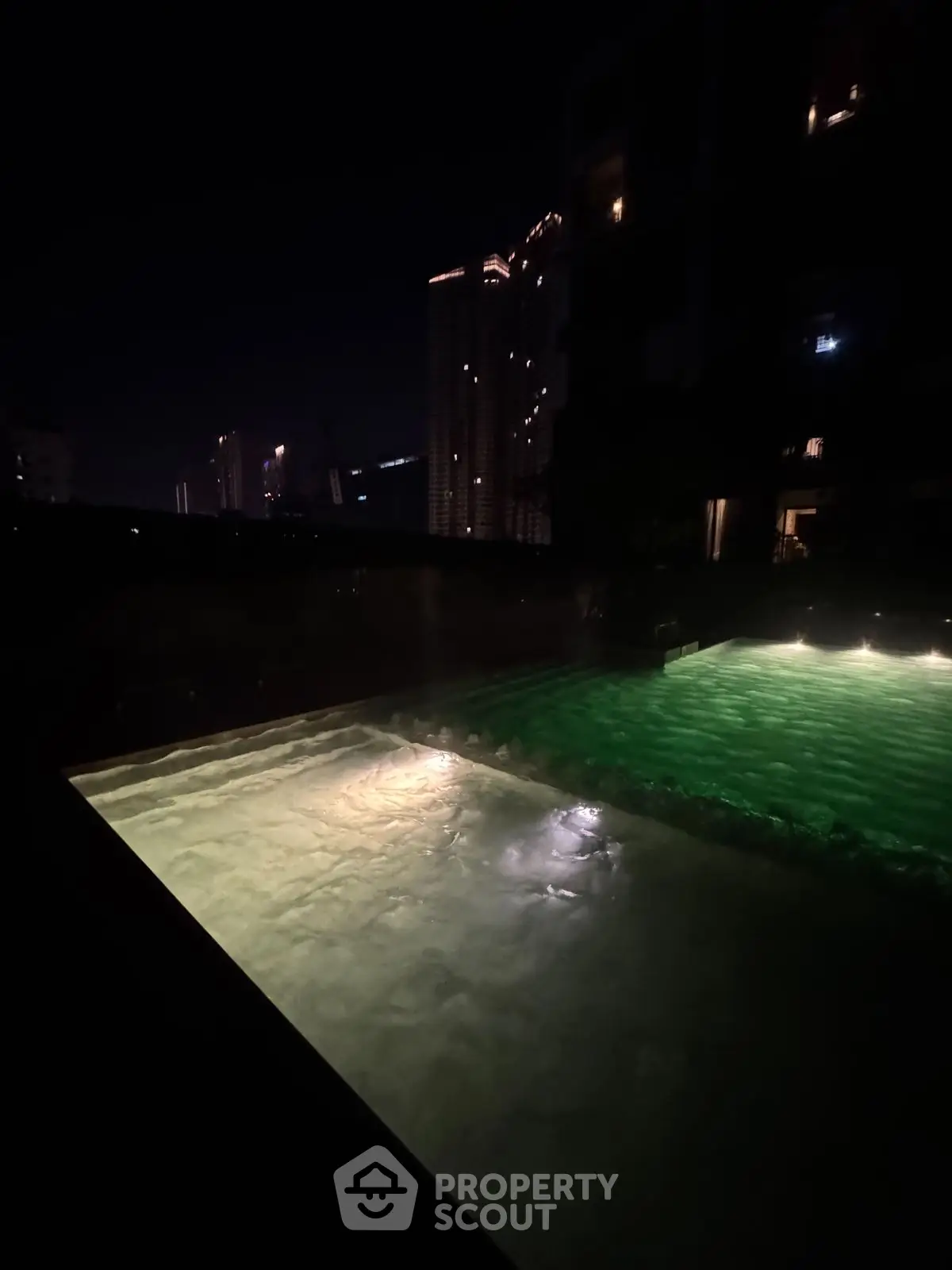 Luxurious night view of illuminated swimming pool with city skyline backdrop.