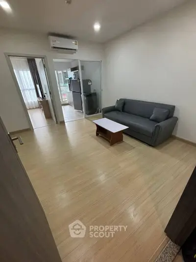 Modern living room with sleek sofa and wooden flooring, adjacent to a bright bedroom.