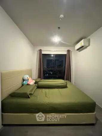 Cozy bedroom with green bedding and city view, featuring air conditioning and plush toys.