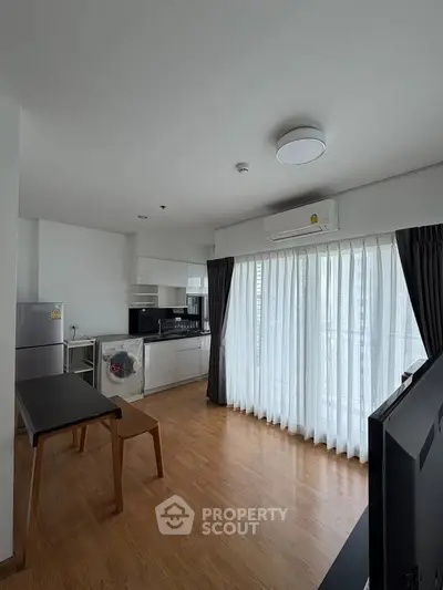 Modern open-layout kitchen with wooden flooring and large windows in a bright apartment.