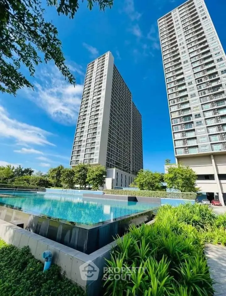 Stunning modern high-rise buildings with a luxurious pool and lush greenery under a clear blue sky.