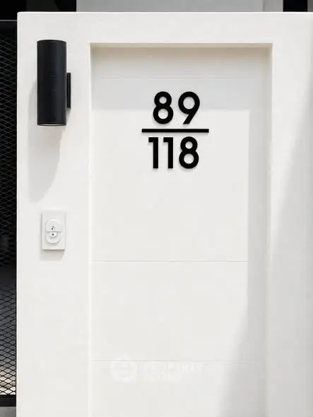Modern minimalist entrance with sleek black wall light and house number 89/118 on white facade.