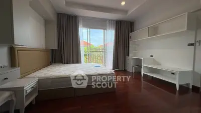 Spacious bedroom with large window and built-in shelves, featuring elegant hardwood flooring.