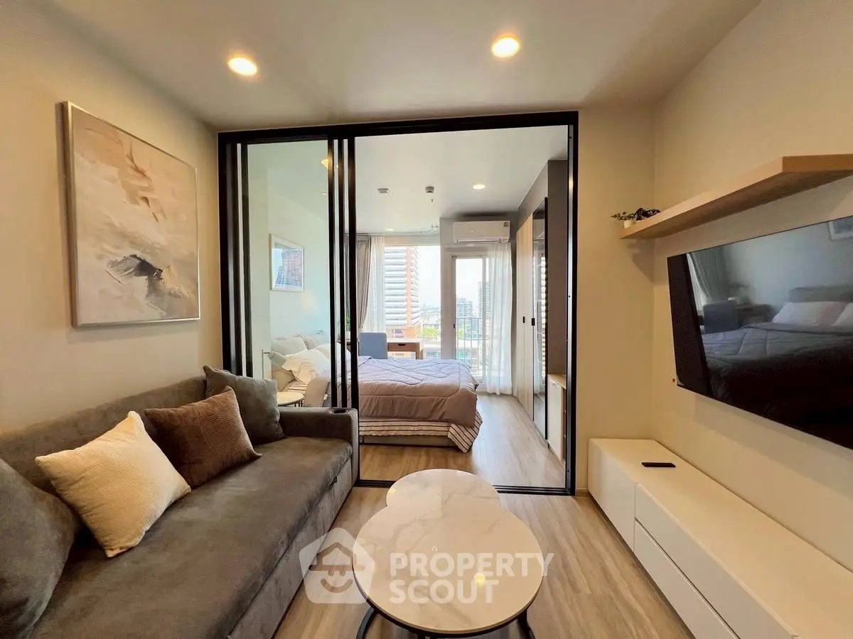 Modern apartment interior with cozy living room and stylish bedroom separated by glass doors, featuring city view.