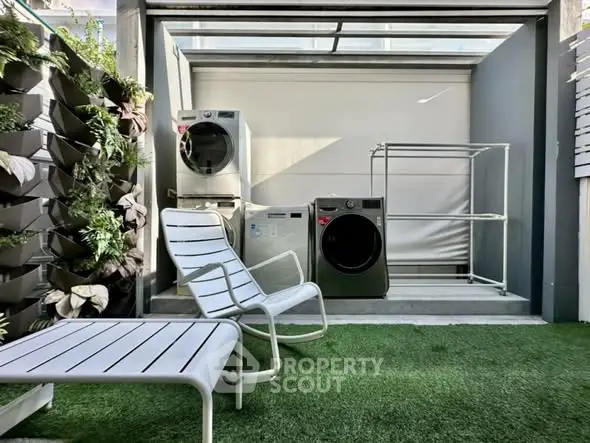 Modern outdoor laundry area with washing machines and seating on artificial grass.