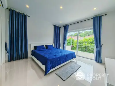 Spacious bedroom with blue decor and large window overlooking greenery