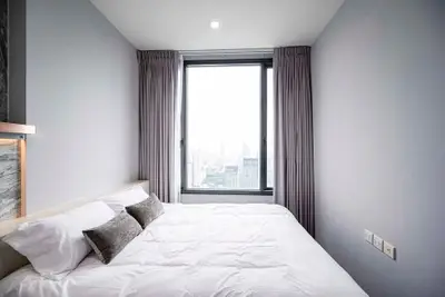 Modern bedroom with large window offering stunning city view, featuring elegant decor and cozy bedding.