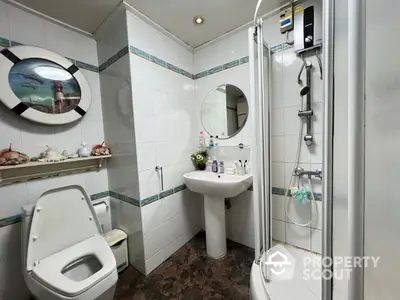 Compact modern bathroom with a corner shower cabin, pedestal sink, and toilet, accented with blue tile trim and mirrored accessories.