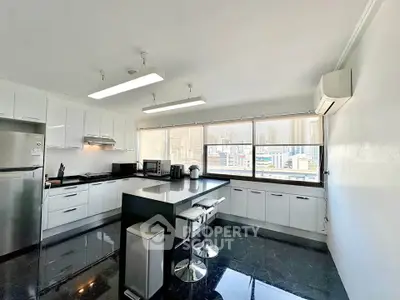 Spacious modern kitchen with city view, sleek black countertops, and white cabinetry in a high-rise apartment.