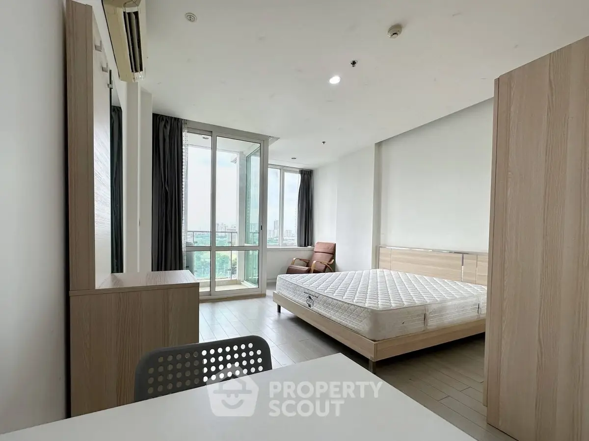 Spacious bedroom with large windows and modern furnishings in a high-rise apartment.