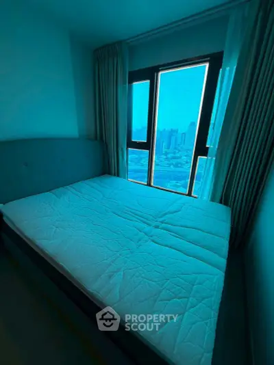 Cozy bedroom with large window offering stunning city views, perfect for urban living.