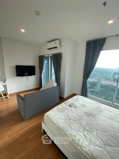 Modern bedroom with large windows and balcony access, featuring a cozy sofa and wall-mounted TV.