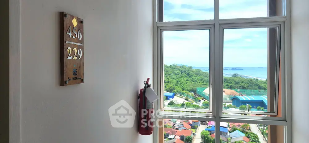 Stunning ocean view from high-rise building window with fire extinguisher and room number sign.