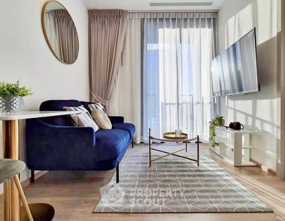 Modern living room with stylish decor, featuring a blue sofa, wall-mounted TV, and large window with sheer curtains.