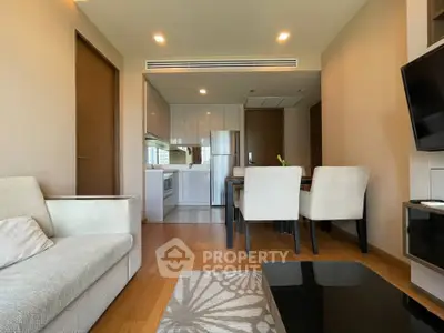 Modern living room with open kitchen and dining area, featuring sleek furniture and wooden flooring.