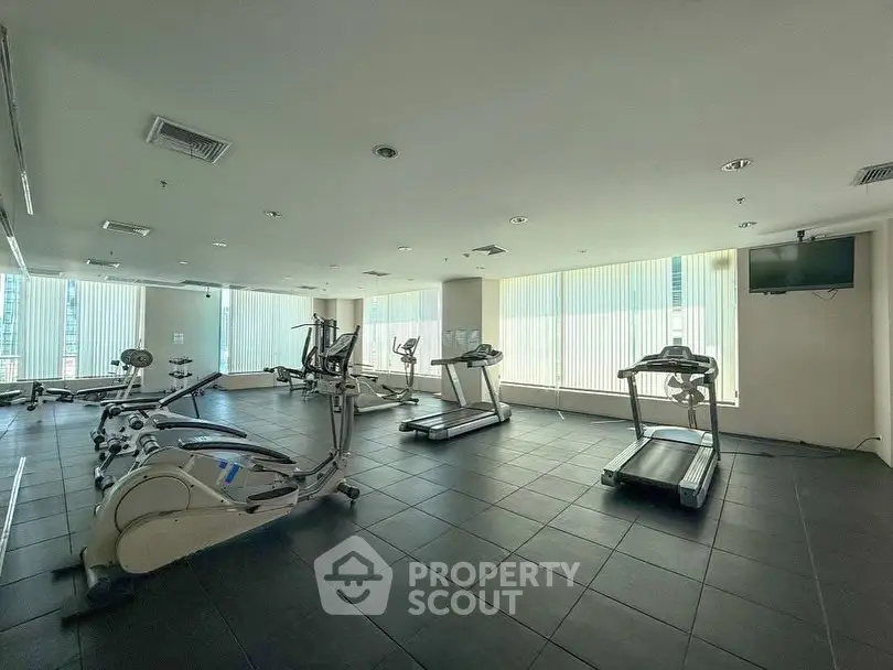 Spacious gym with modern equipment and large windows in a high-rise building.