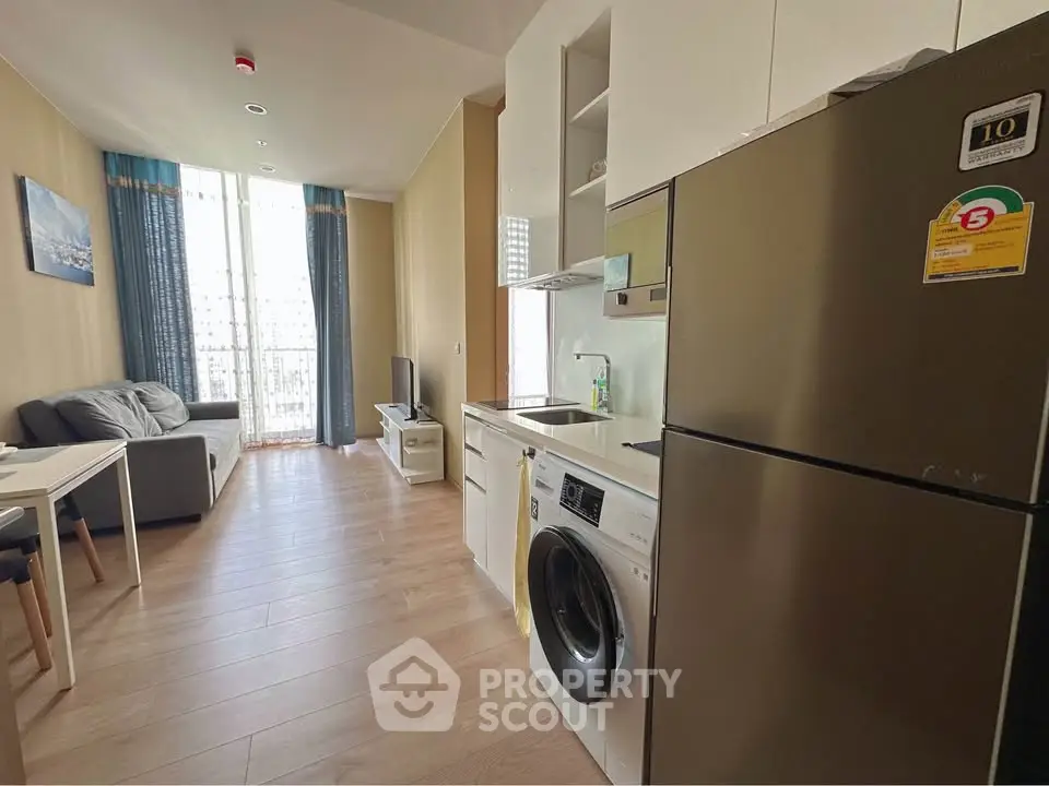 Modern apartment with open kitchen and cozy living area, featuring a washing machine and large windows.