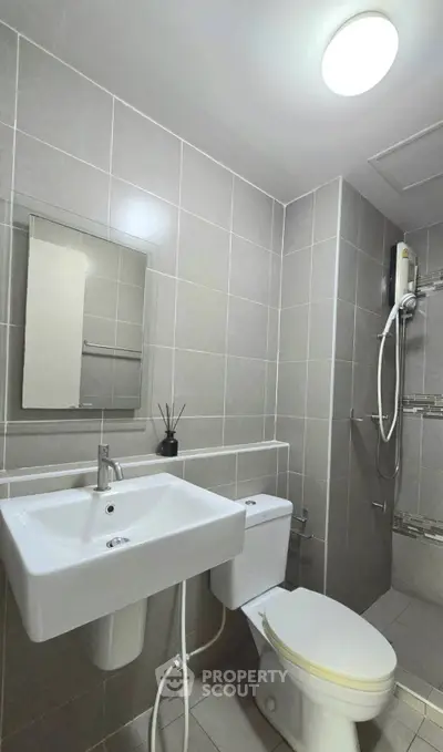 Modern bathroom with sleek fixtures and tiled walls, featuring a shower and a vanity mirror.