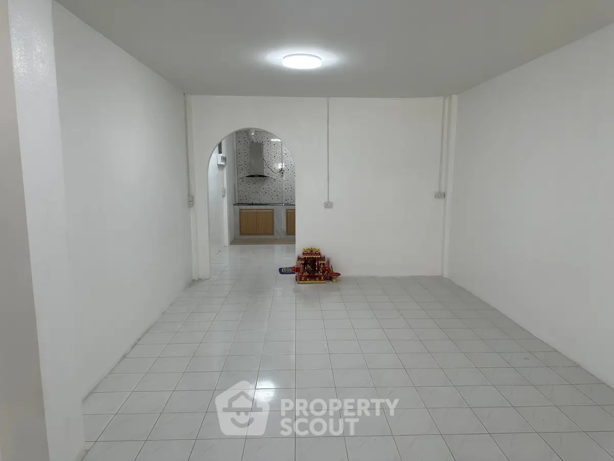 Spacious open-plan living area with tiled flooring and archway leading to kitchen.