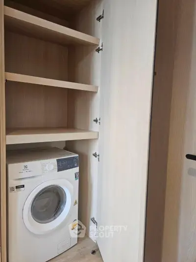 Compact laundry area with built-in shelves and washing machine in modern apartment.