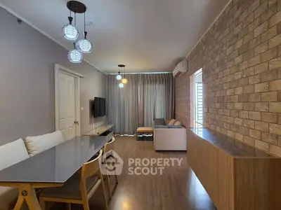 Modern living room with stylish lighting and brick accent wall, featuring a cozy seating area and dining table.