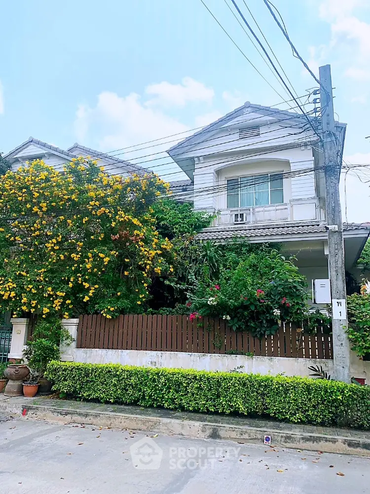 Charming two-story residence surrounded by lush greenery and vibrant flowering shrubs, featuring a classic design with a welcoming ambiance, nestled in a serene neighborhood.