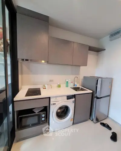 Modern compact kitchen with appliances including washing machine and fridge, sleek cabinetry, and induction cooktop.