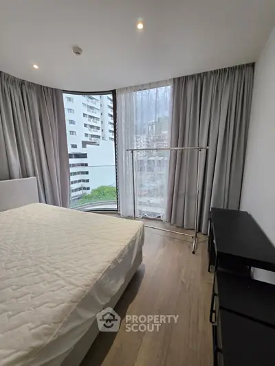 Modern bedroom with large window and city view, featuring sleek furniture and elegant curtains.