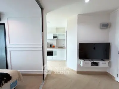 Modern open-plan living room with sleek TV setup and view into minimalist kitchen.