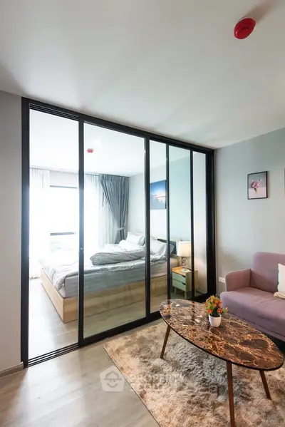 Modern apartment with glass partition separating living room and bedroom, featuring stylish decor.
