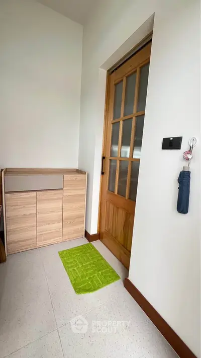 Modern entryway with wooden door and storage cabinet, featuring a green mat for a welcoming touch.