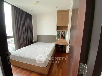 Modern bedroom with wooden flooring and large window offering city views.