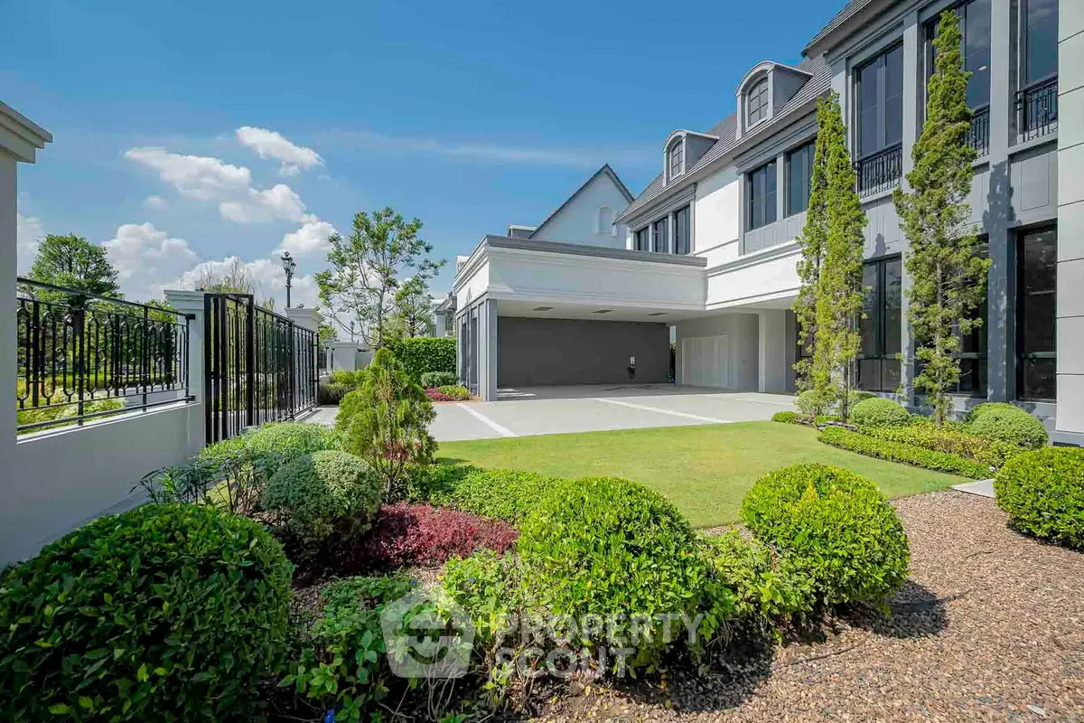 Luxurious modern home exterior with manicured garden and spacious driveway under a clear blue sky.