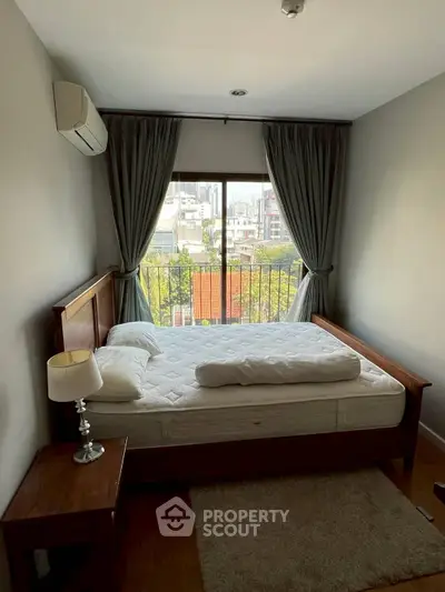 Cozy bedroom with city view, featuring a wooden bed frame, bedside table, and elegant curtains.