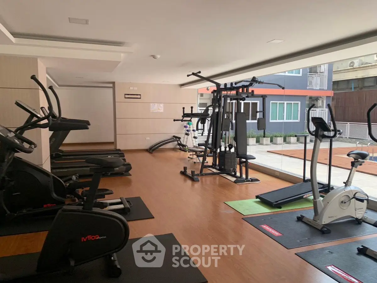 Modern gym with exercise equipment and large windows in a residential building.