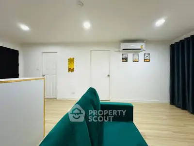Modern living room with green sofa and minimalist decor, featuring wooden flooring and air conditioning.