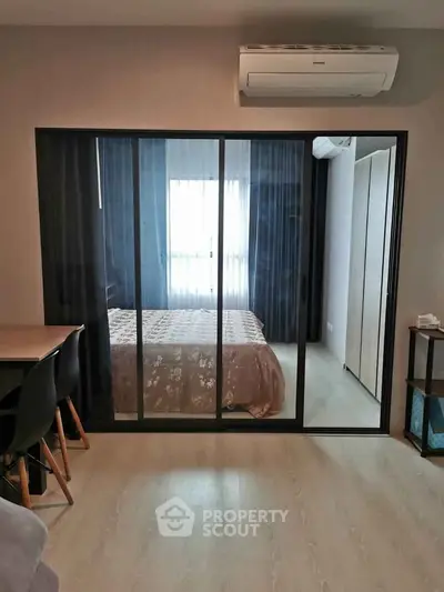 Modern bedroom with sliding glass doors and air conditioning, featuring sleek furniture and natural light.
